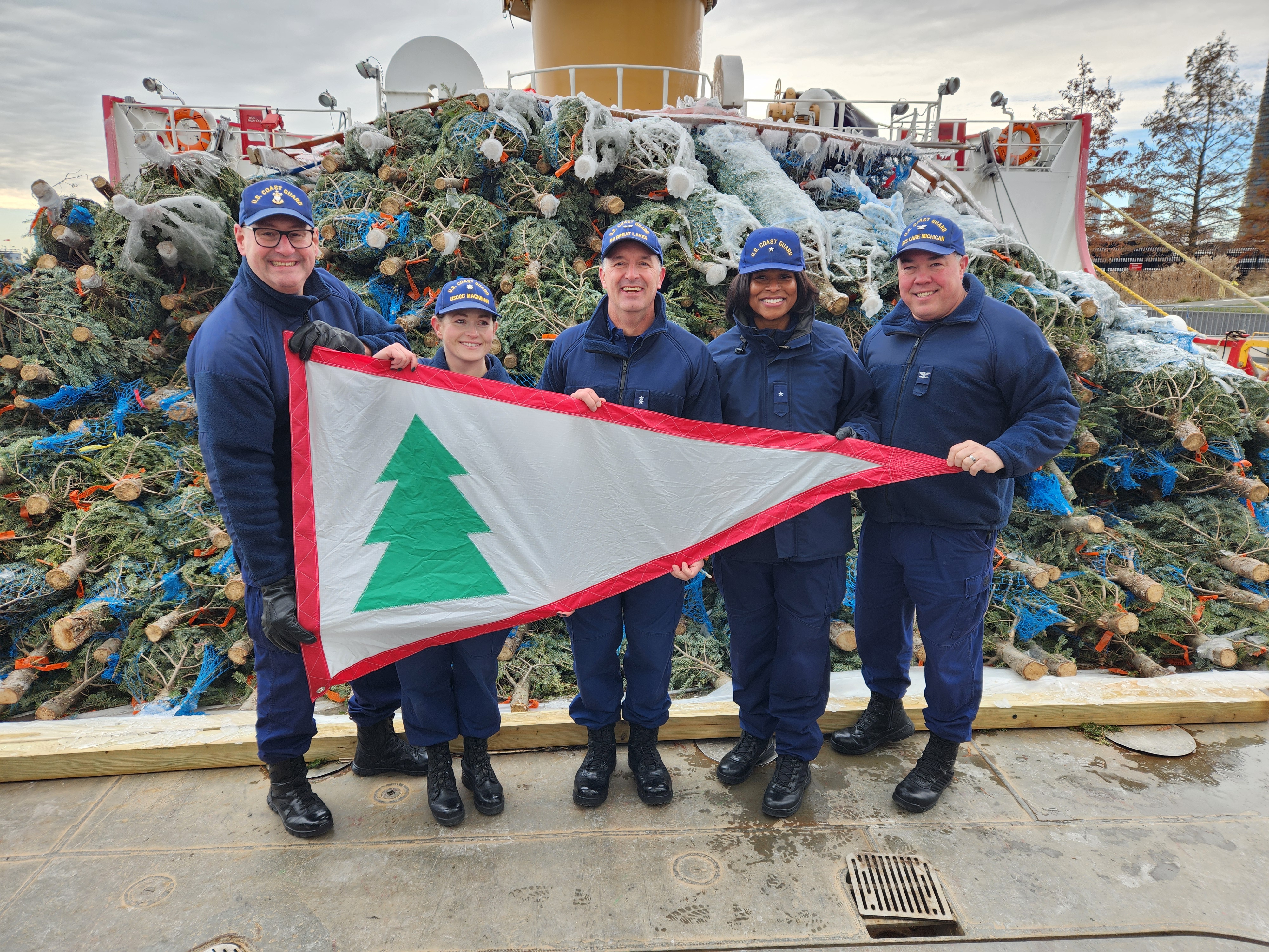 Master Chief Petty Officer of the Coast Guard Heath Jones, Mackinaw Commanding Officer Commander Jeanette Greene, Ninth District Commander Rear Admiral John Hickey, Personnel Service Center Commanding Officer Rear Admiral Zeita Merchant, and Sector Lake Michigan Commanding Officer Captain Seth Parker hold the Christmas Tree Pennant while posing in front of the 1200 Christmas Trees being delivered to Chicago by the USCGC Mackinaw during the Grand Arrival event held before the tree offload the next day. U.S. Coast Guard Photo by AUXPA1 Matthew Thompson Master Chief Petty Officer of the Coast Guard Heath Jones, Mackinaw Commanding Officer Commander Jeanette Greene, Ninth District Commander Rear Admiral John Hickey, Personnel Service Center Commanding Officer Rear Admiral Zeita Merchant, and Sector Lake Michigan Commanding Officer Captain Seth Parker hold the Christmas Tree Pennant while posing in front of the 1200 Christmas Trees being delivered to Chicago by the USCGC Mackinaw during the Grand Arrival event held before the tree offload the next day. U.S. Coast Guard Photo by AUXPA1 Matthew Thompson